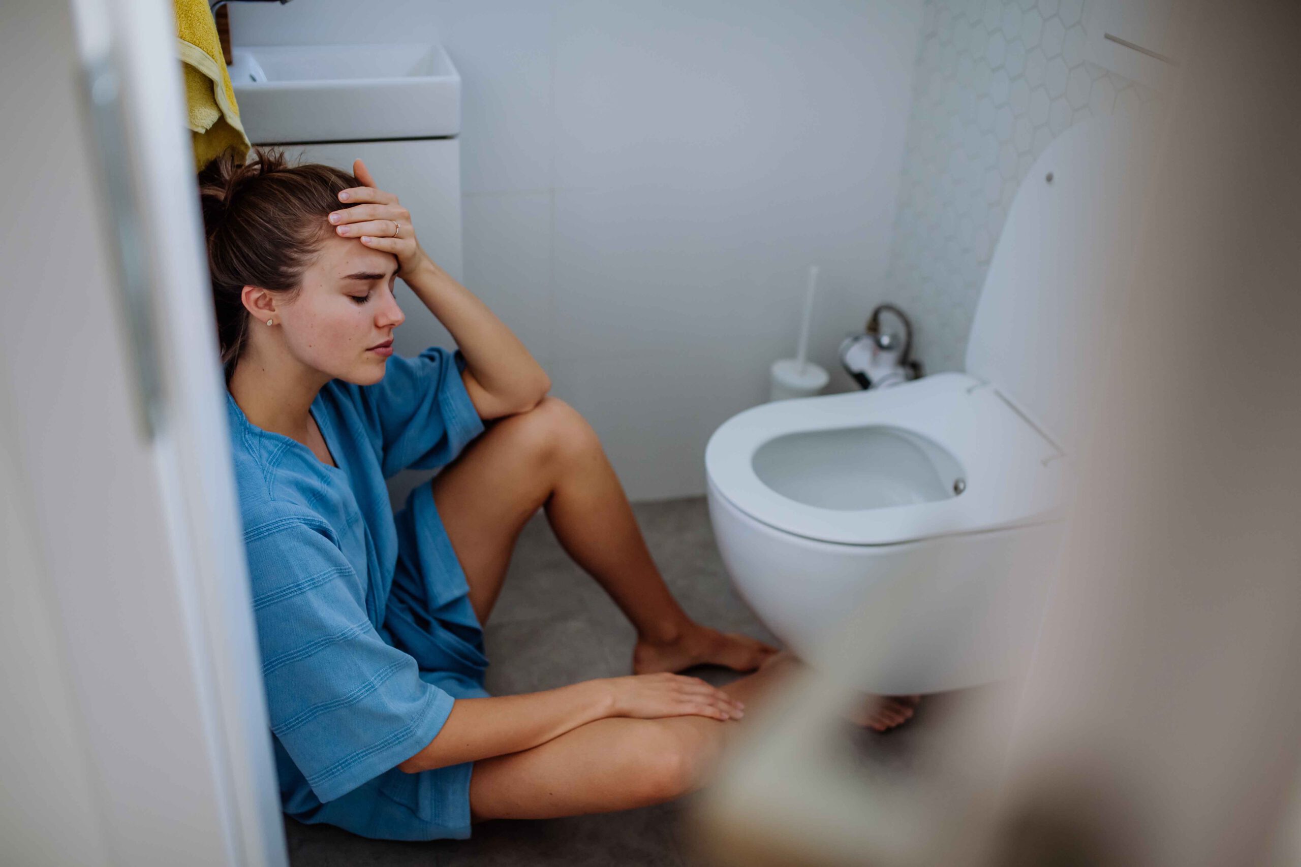 jonge vrouw zit op de grond bij wc overgeven kater.jpg