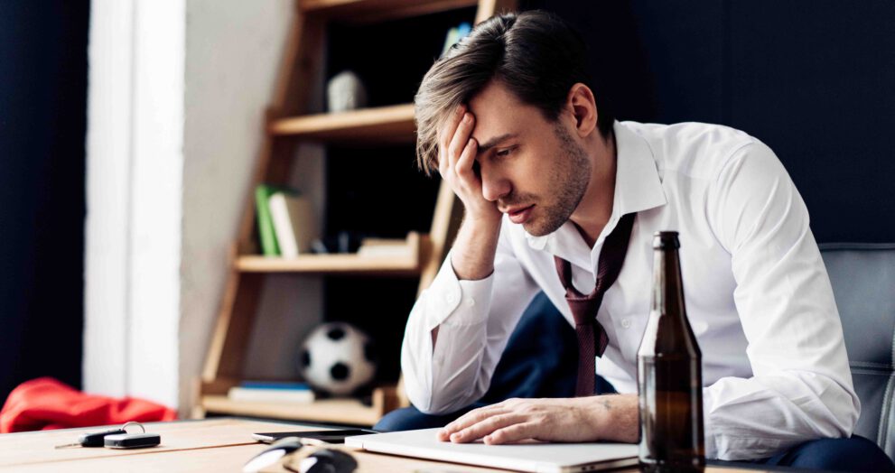 man zit met hoofdpijn kater brak flesje bier computer werk