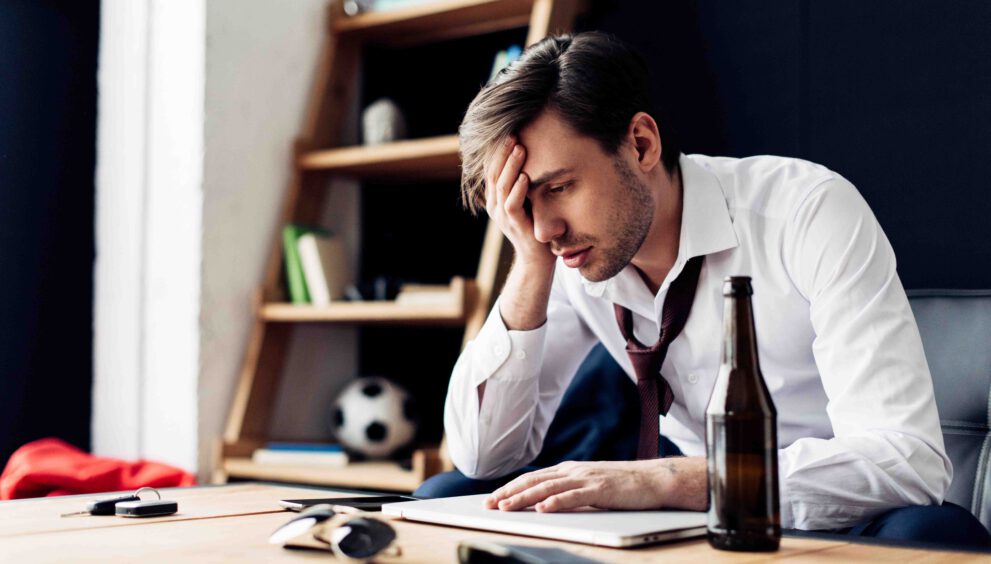 man zit met hoofdpijn kater brak flesje bier computer werk